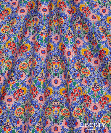 A close-up of draped fabric featuring a dense, colorful Art Nouveau floral pattern with pink, blue, red, yellow, and green motifs.