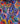 A close-up of a colorful printed fabric with a bold floral and paisley pattern in blue, pink, red, yellow, green, and white, with a visible Liberty Fabrics logo in the bottom right corner.