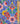A close-up of a colorful patterned fabric with a vertical wooden ruler on the right side for scale. The fabric features a traditional floral and ornamental design in blue, pink, red, green, yellow, and white on a dark background.