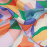 A close-up of draped Liberty Fabrics featuring a colorful geometric pattern with abstract shapes in orange, green, blue, purple, pink, and yellow on a white base.