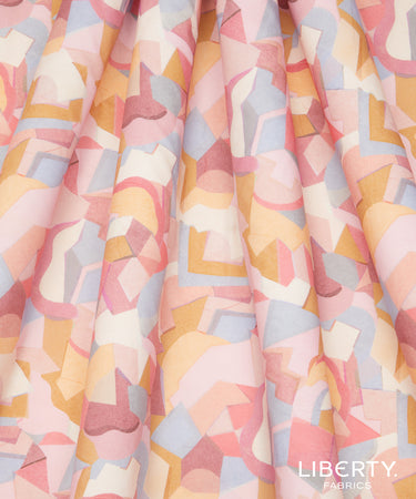 A close-up of draped fabric with a pastel geometric pattern featuring pink, peach, yellow, light blue, and cream shapes. The Liberty Fabrics logo is visible in the bottom right corner.