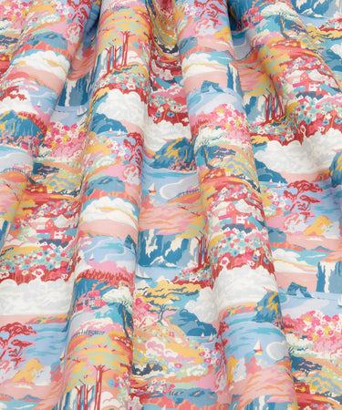 A close-up of draped fabric with a colorful scenic print featuring mountains, clouds, trees, flowers, and stylized figures in pink, blue, white, yellow, and orange tones.