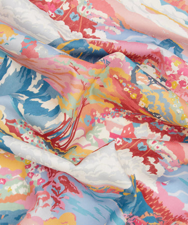 A close-up of a lightweight fabric with a colorful coastal print in a mix of pink, blue, yellow, red, and white tones, and laid in soft folds.