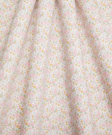 A close-up of a light floral fabric with small pink and yellow flowers, showing soft folds and texture.