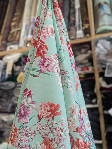 Floral fabric with pink and red flowers on a pastel background, draped in a store setting.