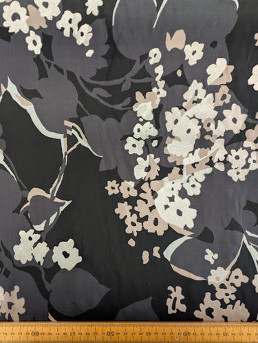 Silk chiffon fabric with a foil printed floral design in champagne, silver and grey on a black base, shown with a ruler at the bottom for scale.