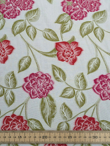 Floral fabric pattern with red flowers and green leaves on a white background, shown with a ruler for scale.