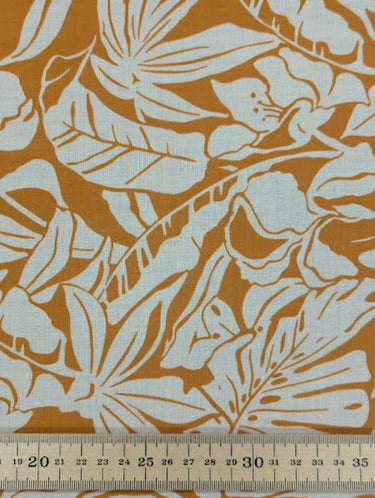 Close-up of a printed pure cotton fabric with ivory botanical print on a mustard base, featuring a ruler at the bottom for scale.