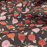 A close up view of silk satin fabric with a floral pattern in shades of red and copper on a brown background.