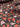 A close up view of silk satin fabric with a floral pattern in shades of red and copper on a brown background.