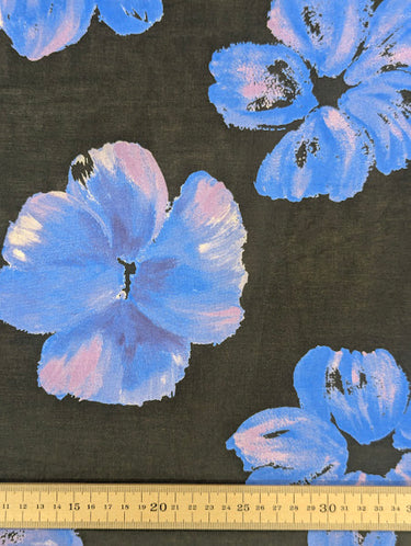 A printed pure cotton fabric, with floral patterns in blue and lilac on a black base, featuring a ruler at the bottom for scale.