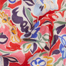 A close-up of draped Liberty Fabrics featuring a vibrant floral pattern with red, pink, blue, purple, green, and yellow motifs on a white base.