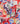 A close-up of draped Liberty Fabrics featuring a vibrant floral pattern with red, pink, blue, purple, green, and yellow motifs on a white base.