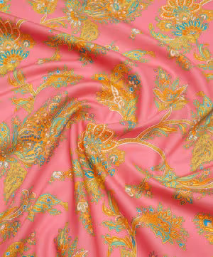 Pink fabric with an ornate paisley and floral pattern in gold, teal, and orange, draped to show its texture and sheen.
