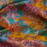 A close-up of draped Liberty Fabrics featuring a vibrant, multicolor floral and botanical print with a deer motif. The print showcases a rich palette of teal, mustard yellow, dusty pink, burgundy, and orange, with the 'LIBERTY.