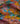 A close-up of draped Liberty Fabrics featuring a vibrant, multicolor floral and botanical print with a deer motif. The print showcases a rich palette of teal, mustard yellow, dusty pink, burgundy, and orange, with the 'LIBERTY.