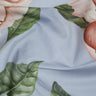 A close-up of light blue fabric printed with large pink flowers and green leaves, with the Liberty Fabrics logo in the bottom right corner.