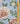 A close-up of a floral fabric print featuring large pale pink peonies and green leaves on a light blue background, with a wooden ruler along the right side and a visible Liberty Fabrics logo at the bottom right.