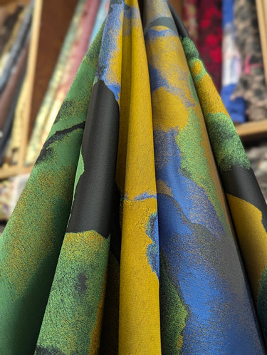 Colourful patterned fabric with green, yellow, and blue colours, draped within a store setting.