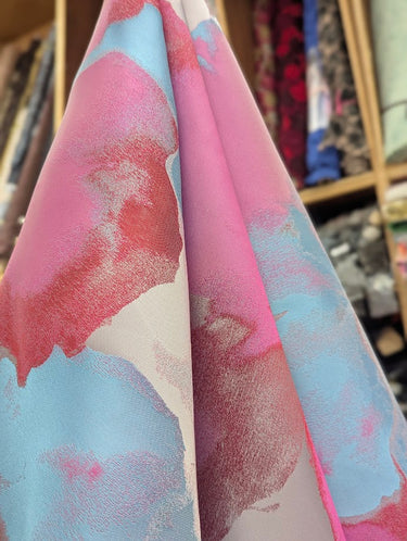 Close-up of textured fabric with pink, red and blue draped within a store setting