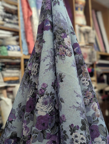 Floral fabric with purple and grey flowers on a light blue background, displayed in a store setting.