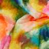 A close-up of colorful tie-dye or watercolor-patterned fabric with blended shades of yellow, pink, blue, green, orange, and white. The Liberty Fabrics logo appears in the bottom right corner.