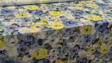 A floral patterned fabric in shades of blue and green shown unrolled on a table 