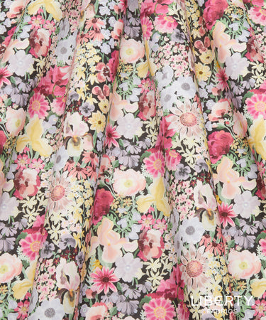 A close-up of a pleated fabric with an all-over multicolor floral print, featuring pink, yellow, white, and red flowers on a dark background. A 'UBERTY' brand watermark is visible in the bottom right corner.
