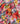 A close-up of draped fabric featuring a vibrant watercolor floral print on a dark navy background. The print includes large flowers in pink, red, orange, yellow, and white, interspersed with green leaves and purple accents.