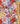 A close-up of a colorful floral fabric print with a gold ruler on the right side for scale. The pattern features a dense mix of wildflowers in red, pink, yellow, blue, purple, and orange on a dark navy background.