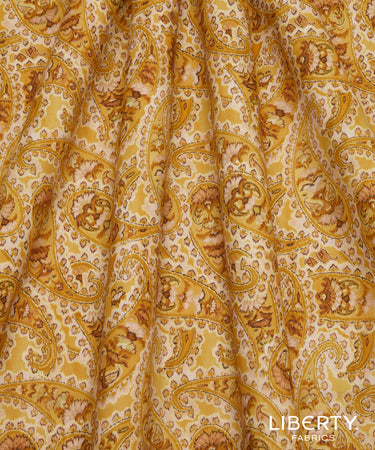A close-up of Liberty Fabrics featuring a classic paisley pattern in mustard yellow, brown, and cream.