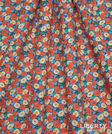 A close-up of a fabric surface with an allover floral print. The pattern features orange-red roses, white daisies with yellow centers, and small green leaves on a blue background.