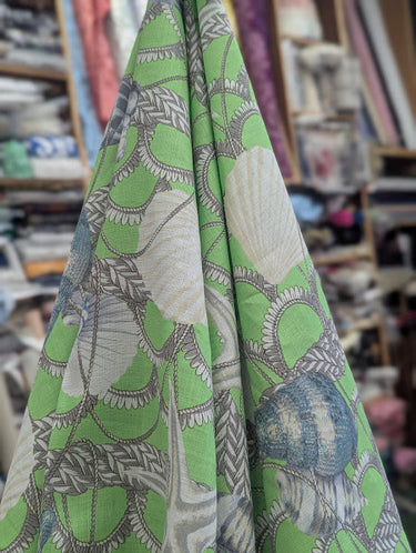 Fabric with nautical pattern featuring shells and ropes on a green background draped in a store setting