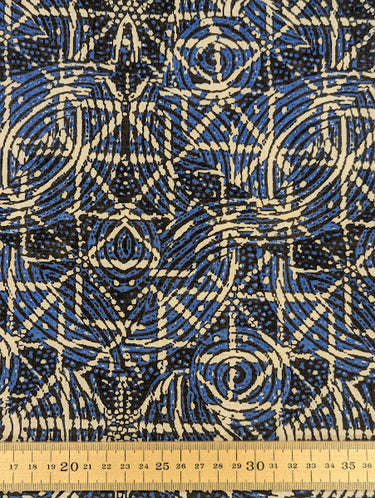 Close-up of a printed pure cotton batiste, with a geometric motif in cobalt blue, ivory, and black, with interlocking circles and angular lines, featuring a ruler at the bottom, for scale.