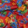 A close-up of a red fabric with a vibrant floral print featuring blue, yellow, and orange flowers with green leaves. The fabric is draped to show its texture and pattern, with a 'LIBERTY FABRICS' logo in the bottom right corner.