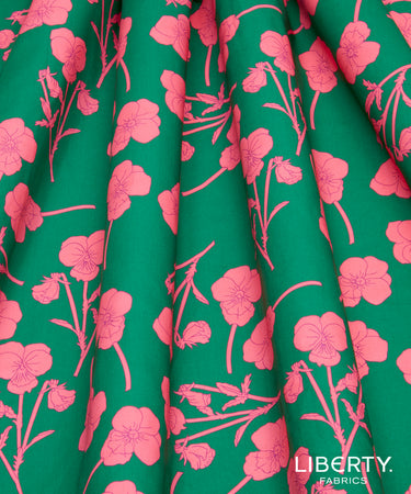 A close-up of Liberty Fabrics floral patterned fabric, featuring a vibrant green background with a bright pink floral print. The fabric is draped in soft folds, showcasing its texture and weight.