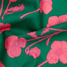 A close-up of green fabric with a bright pink floral print, featuring large flowers and buds with the text 'LIBERTY. FABRICS' in the bottom right corner.