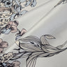 A close up of Silvene 100% Silk Satin fabric with a floral pattern in a grey, blue and white colour range, showing the material's sheen and weave.