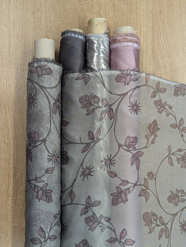 Rolls of plain fabric matching the colours within the printed floral patterns of the silk shimmer chiffon, shown on a shop table