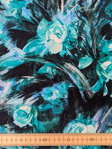 Pure wool fabric with abstract painterly florals in green, black and blue shown with a ruler at the bottom for scale.