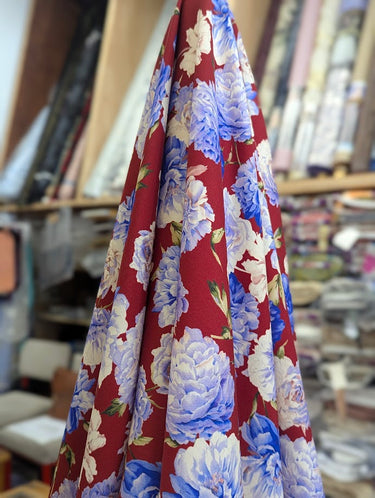 Printed pure wool fabric with blue and white floral pattern on a red background, displayed within a shop setting.