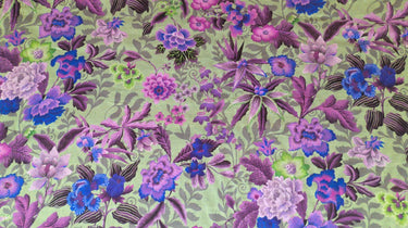 A linen fabric with a bold floral print featuring primarily blue, pink and grey colours on a green background.