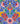 A close-up of a colorful Liberty Fabrics patterned fabric featuring a symmetrical, hand-drawn style floral and scroll design in blue, pink, red, green, yellow, and purple.